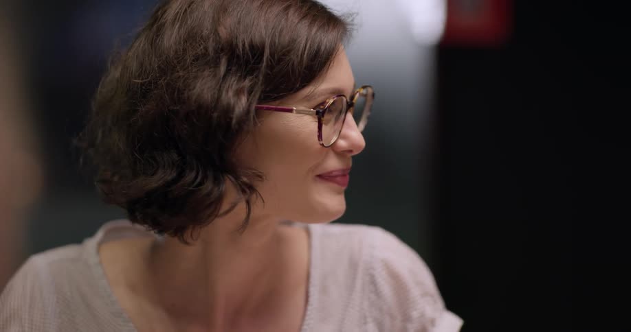 A female wearing tortoise framed glasses takes a sip of a drink while smiling and talking at the table