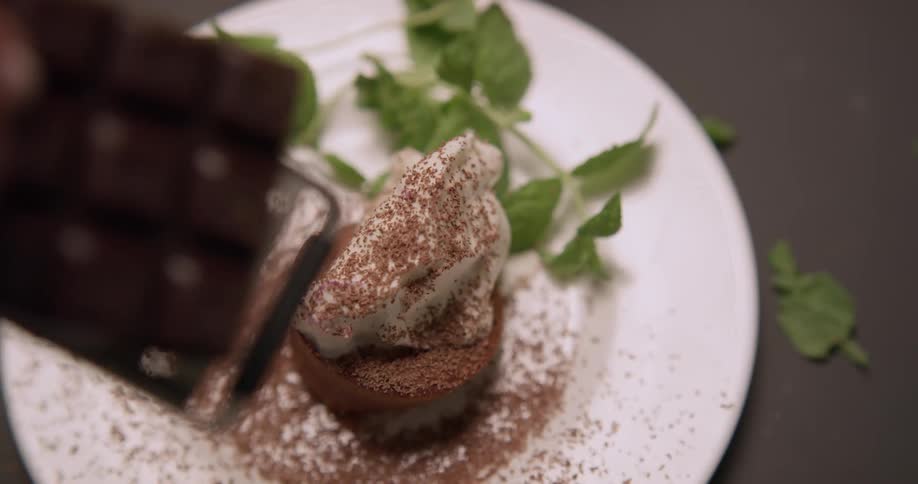 A chef grates chocolate over a plated dessert