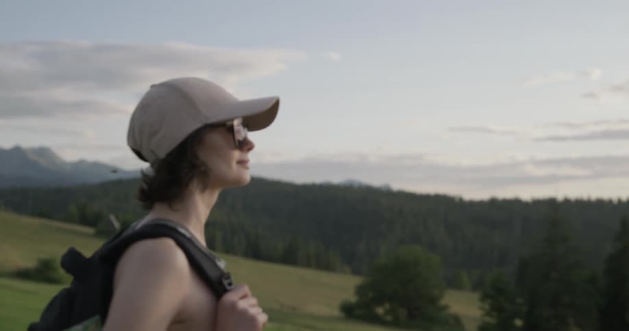A woman with a backpack stands on a hill looking around