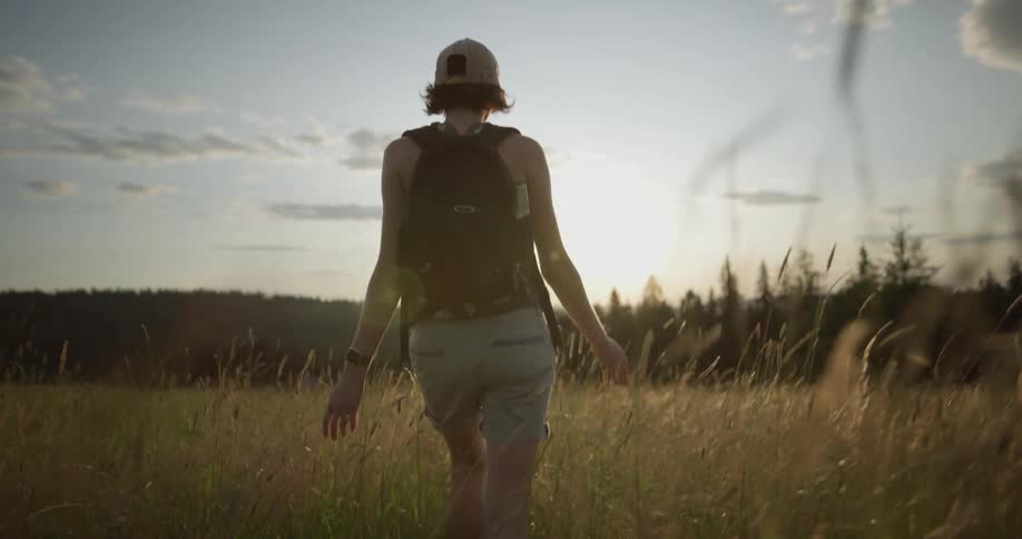 A woman in a hat walks through a field at sunset