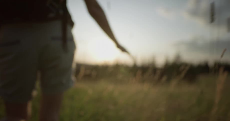 A woman wearing a backpack walks through tall grass