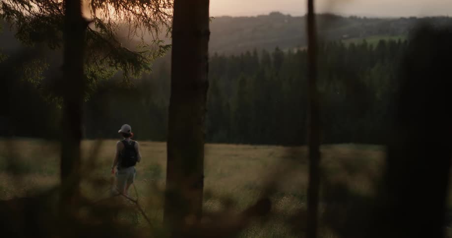 A woman walking through a grass field by a forest