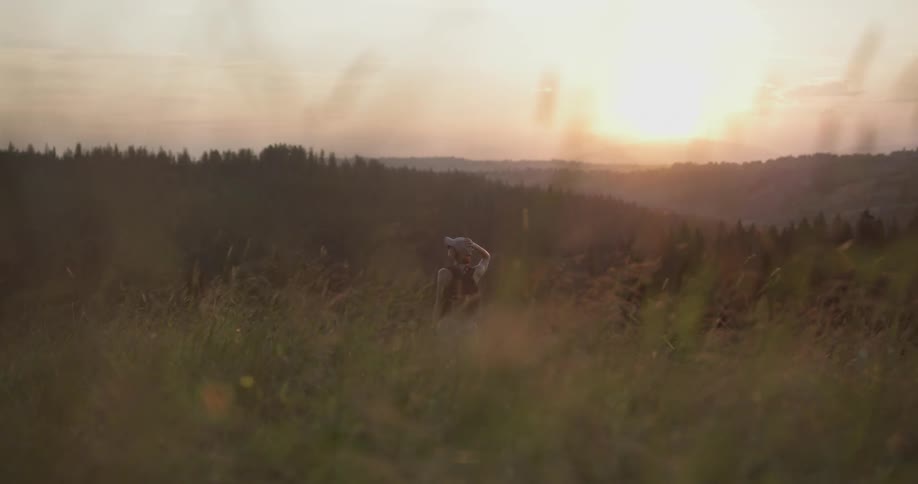Woman wearing cap walks on grassland and take a look at sunset