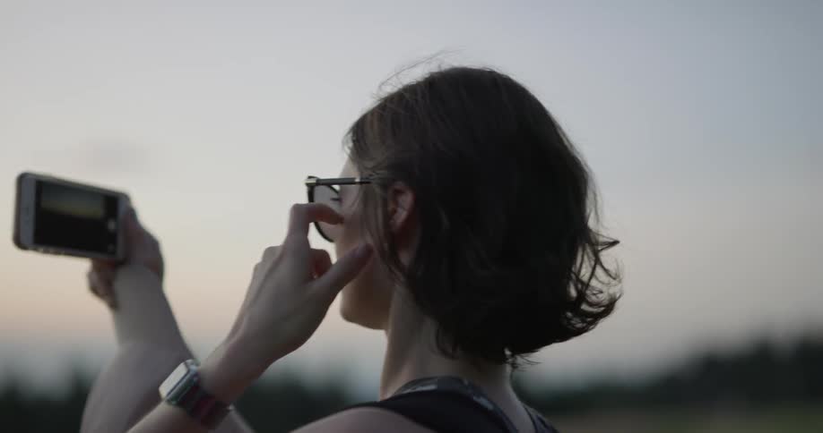 A woman films a sunset on her phone