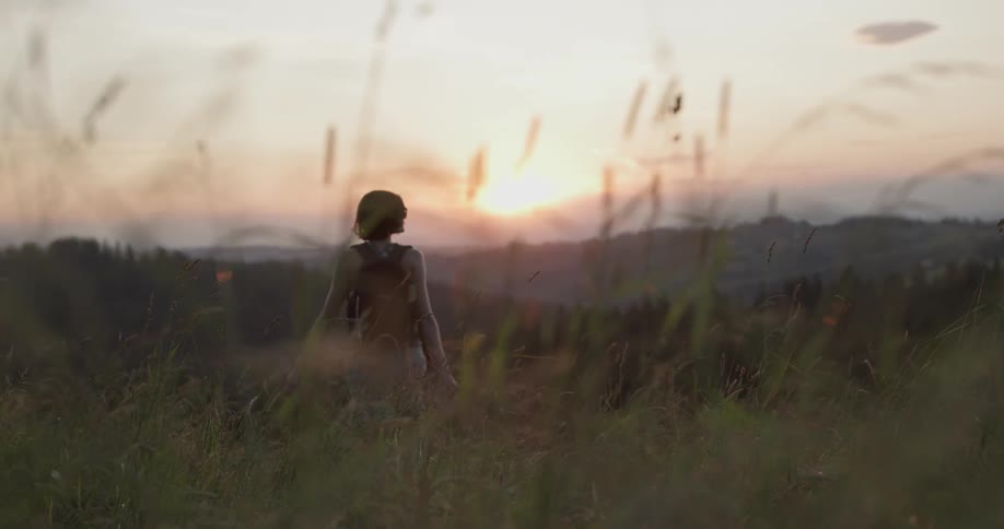 A female hiker walking through a field in the hills at sunrise