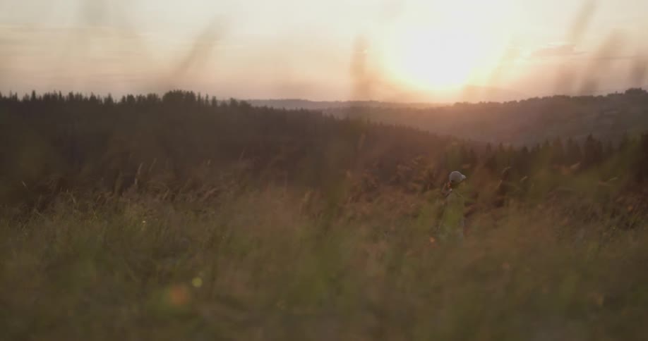A person walking in the wilderness with the sky and the sun in the background