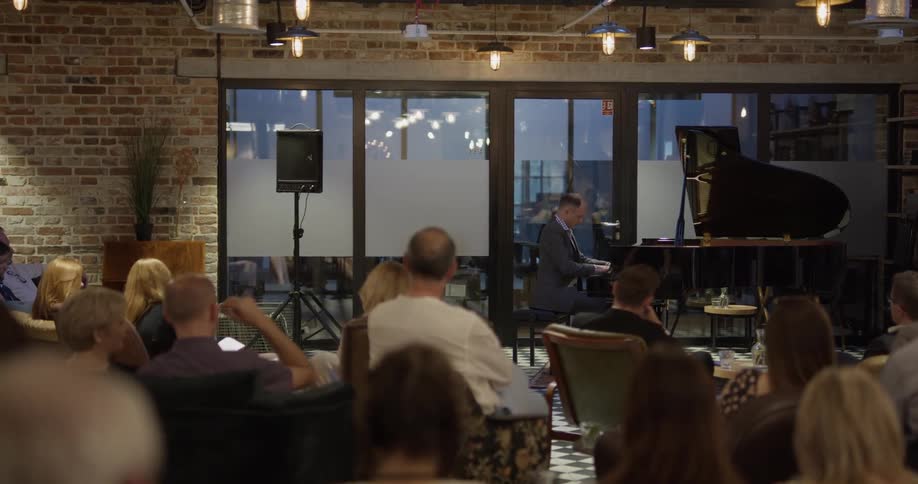 A man plays the piano for an audience sitting in lounge chairs