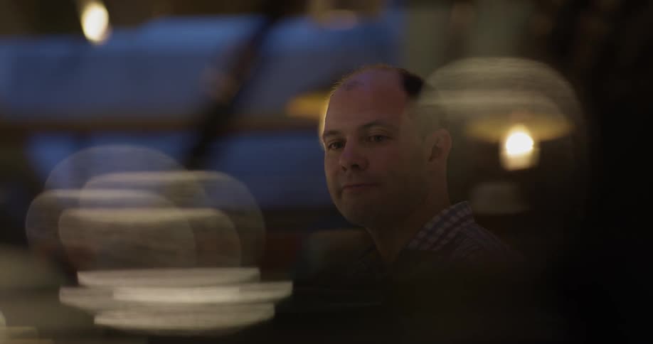 Bald man stands and talks in a dim light room