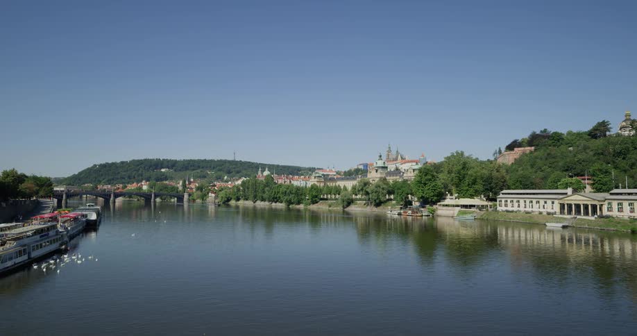 A river cutting through a scenic town with a castle on a hill