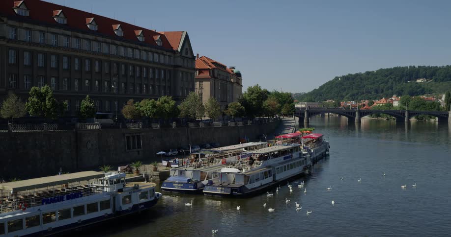 Several large passenger boats are seen docked along the side of a river in a rustic looking european town