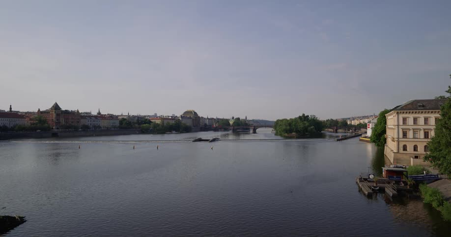 A calm river can be seen flowing under a bridge and between halves of an old style european town