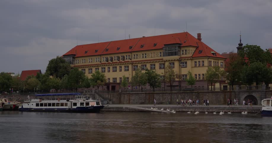People walk towards a ferry docked on the river in an old european town