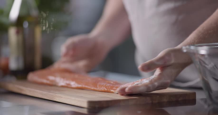 A man takes a slab of fish meat out of a clear glass bowl and spreads it out on a cutting board