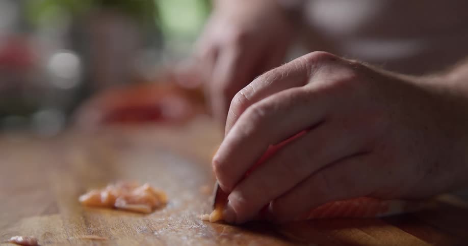 Man cuts fish on the cutting board in the kitchen during daylight