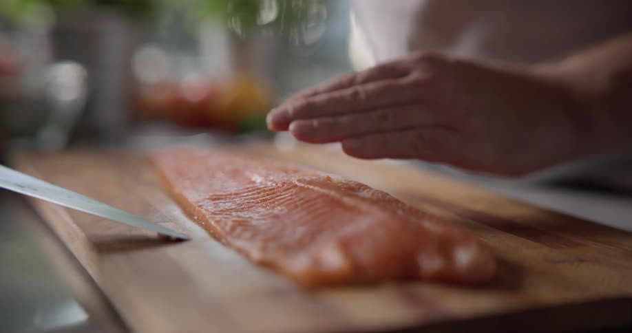 A fish fillet being sliced in half on a cutting board