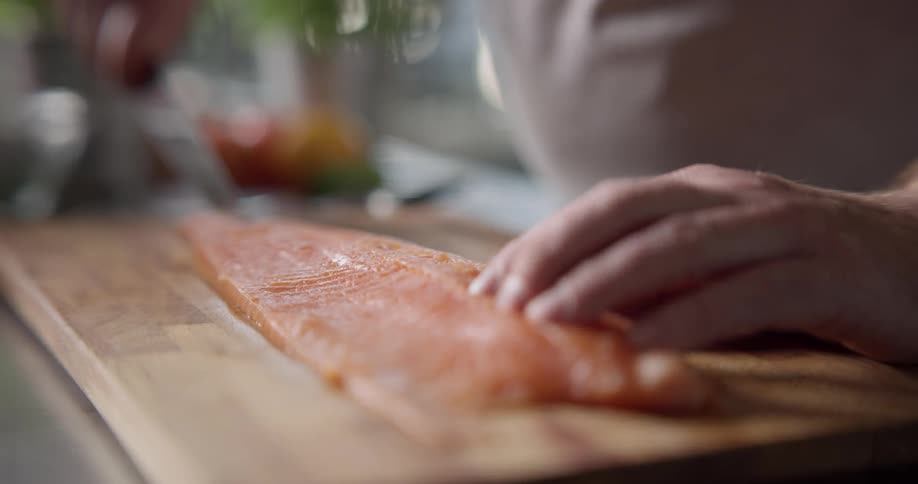A fish fillet being sliced down the middle on a wooden cutting board