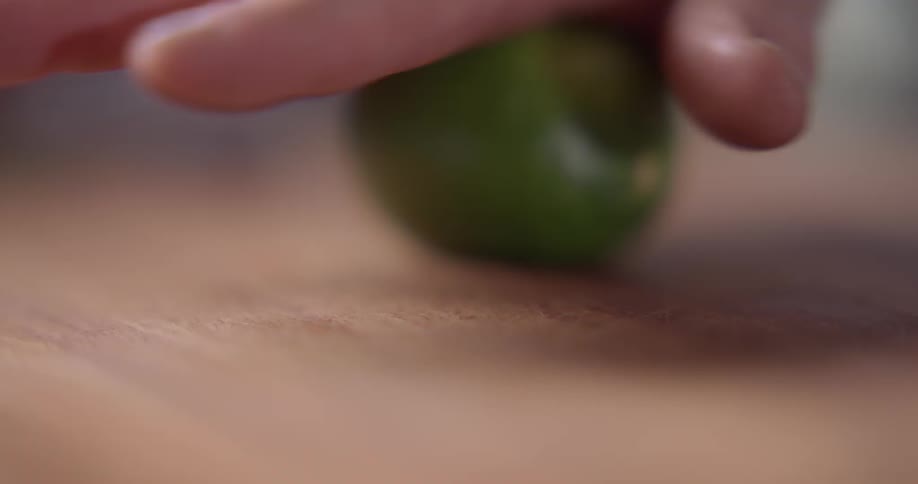 A hand rolling a lime on a wooden surface