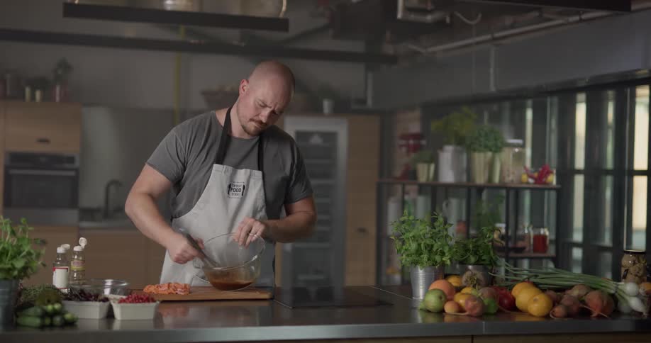 A chef pours sauces from bottles into a mixing bowl then uses a whisk to mix the liquids and places chopped meat into the bowl of liquid