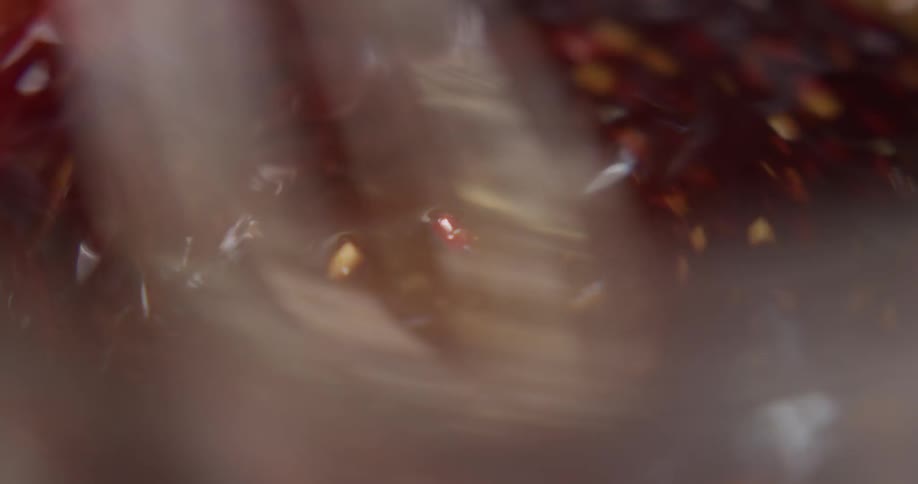 A brown liquid mixture with small sesame seeds and other particulates in it is being mixed and stirred by a metal whisk