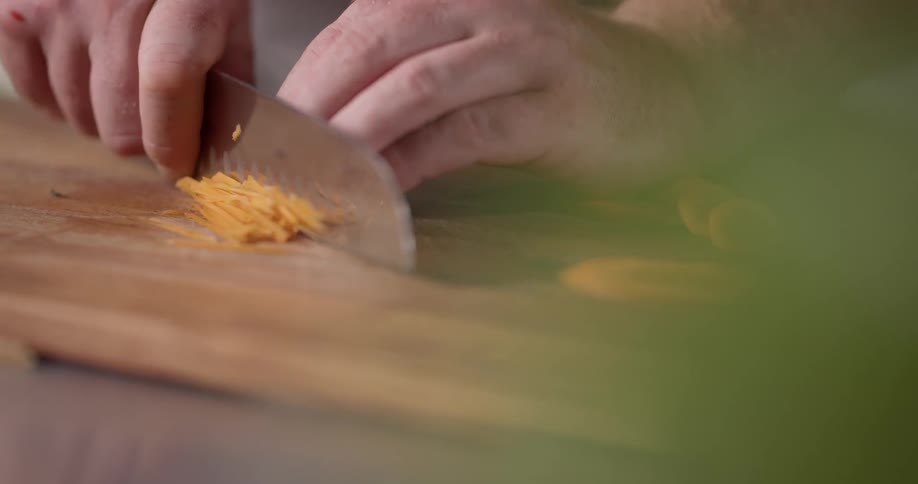 Cook thinly slicing stacked carrots with a large knife on a cutting board