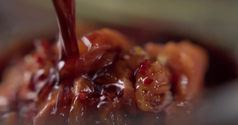 A chef pours a marinade over a bowl of food