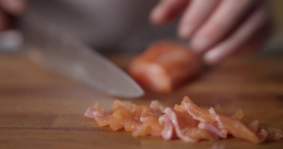 Chef cutting slices of salmon with a knife on a chopping board