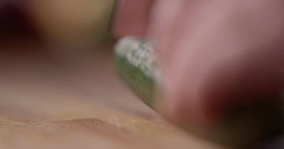 A man uses a sharp knife to slice a cucumber in half on a wood cutting board