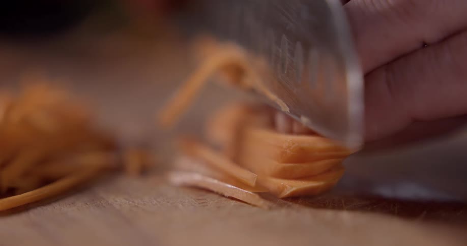 Carrots being sliced on a wooden cutting board