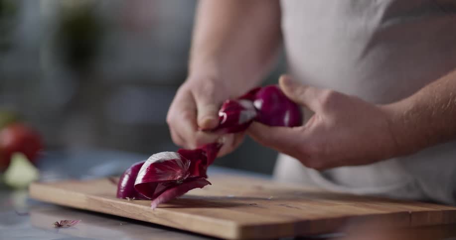 A man peeling an onion on a cutting board