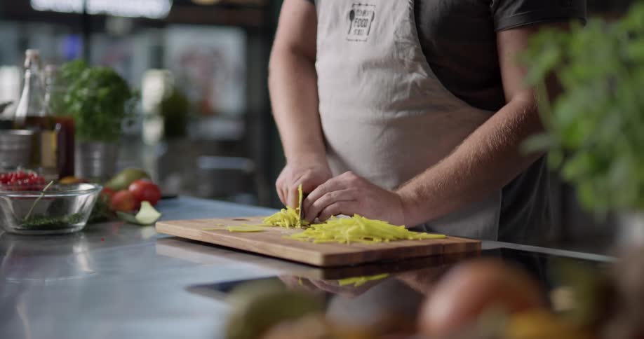 Bald headed man cuts vegetable on cutting board in the kitchen during daylight