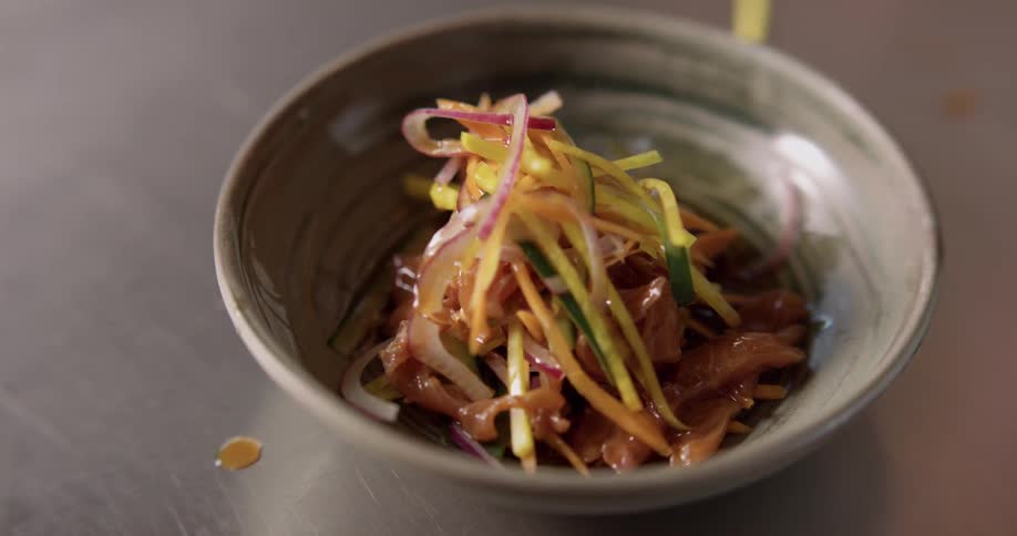 Someone ladles the sauce and arranges vegetables in a small bowl