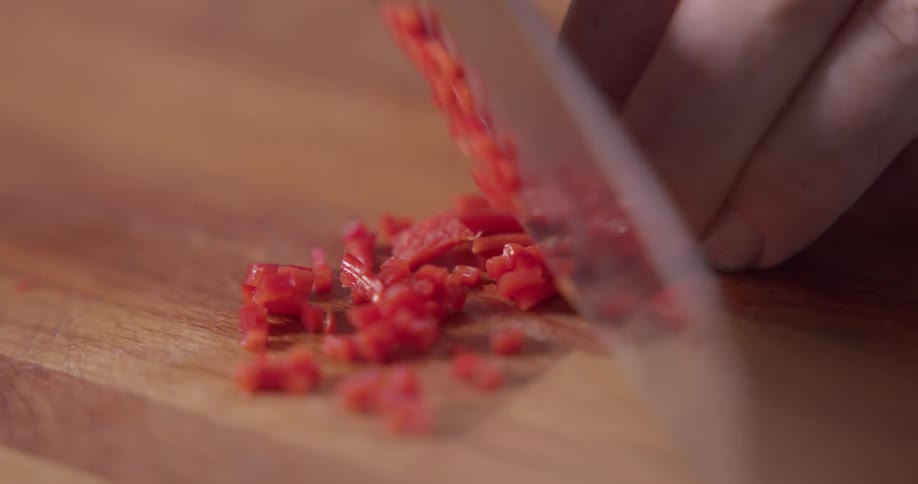 A chef finely dices a red vegetable on a butcher block cutting board