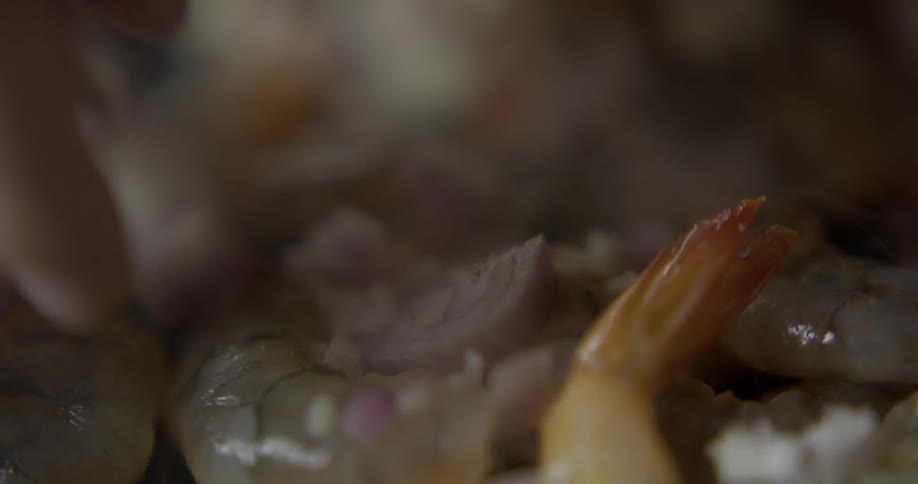 Chef spreads pieces of an onion over a cooking shrimp