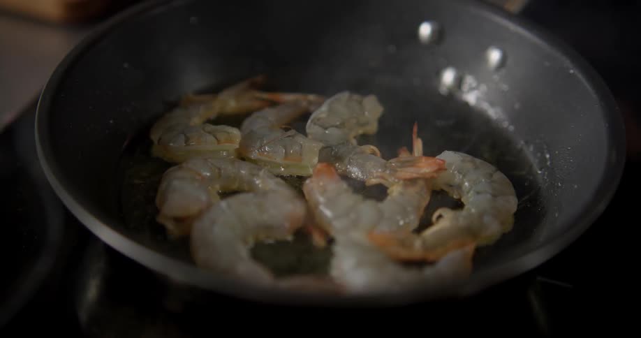 Man fried shrimp in pan on stove in the kitchen