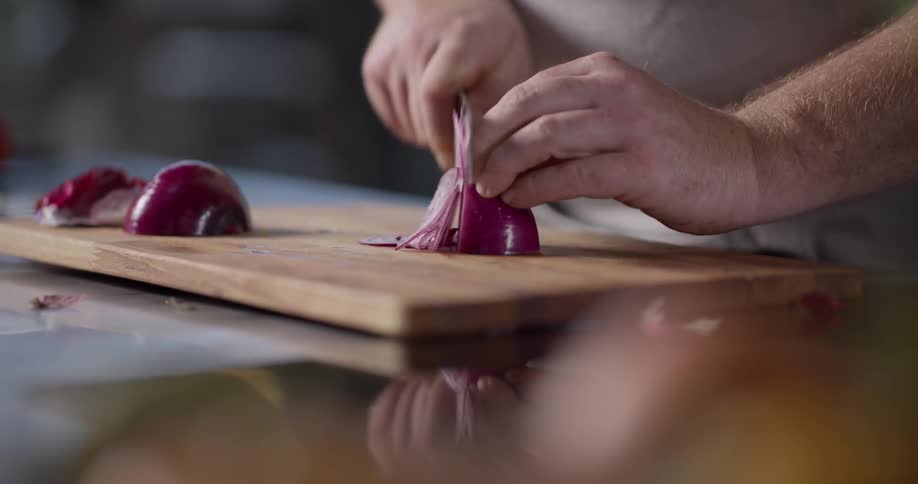 A man uses a sharp knife to slice red onion on a wood cutting board