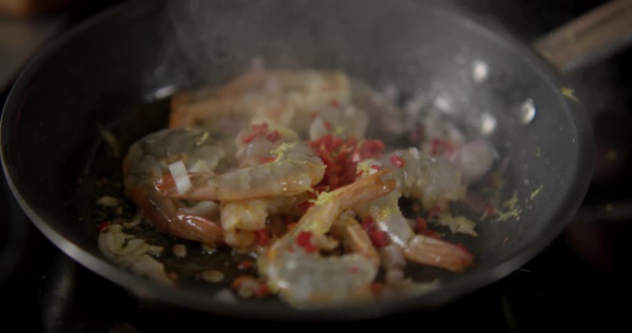 Shrimp and herbs being tossed in a hot skillet