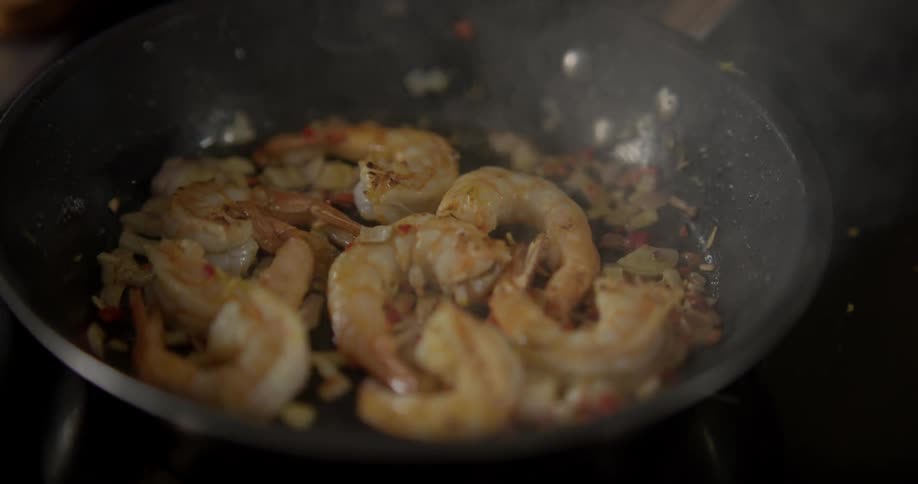 A chef shakes a steaming pan with shrimp cooking in it