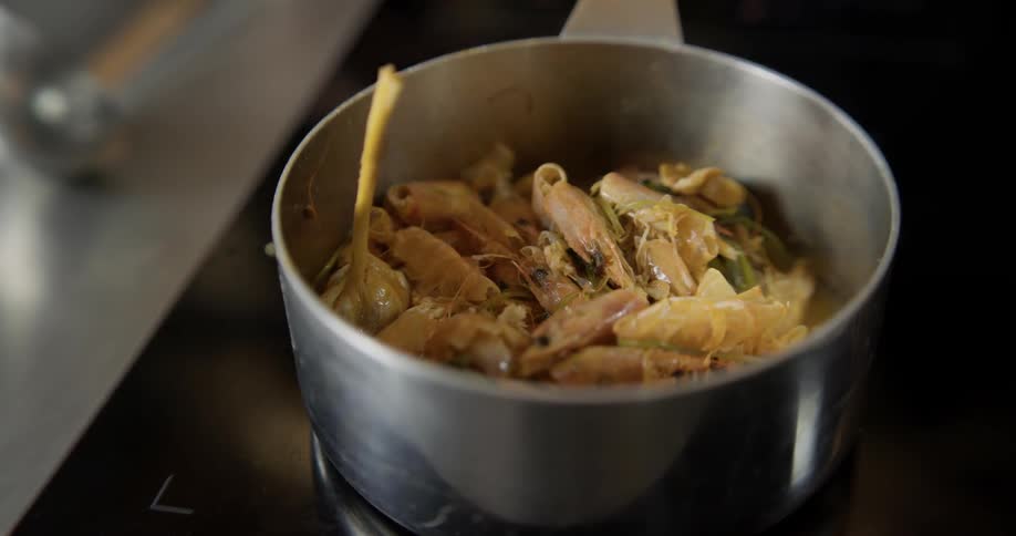A chef pours wine into a pot and mixes it with pasta