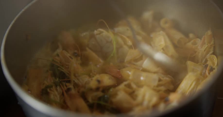 Shrimp cooked in the saucepan is stirred by spoon on the stove during daylight