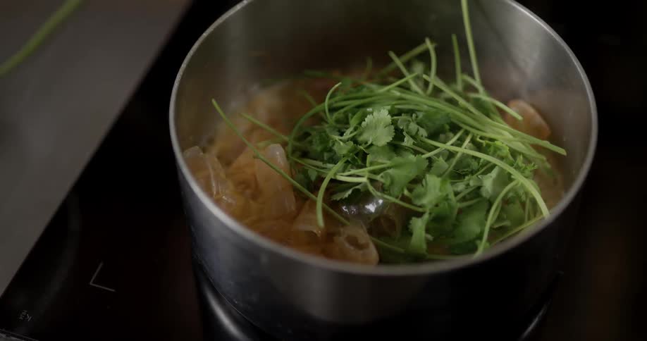 Man puts parsley on shrimp cooked in the saucepan on the stove in the kitchen during daylight