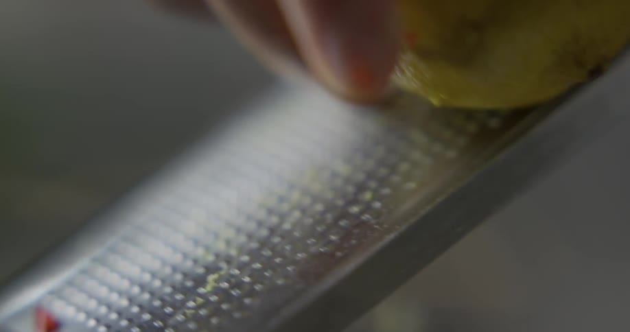 A person uses a grater to shave lemon zest from a lemon