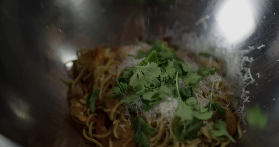 A bowl of pasta being garnished with vegetables