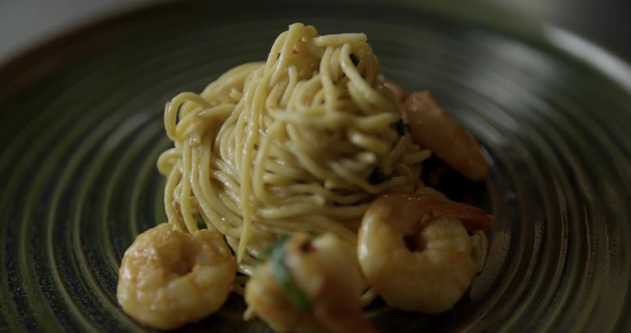 A twirled mound of pasta on a plate has shrimp around it