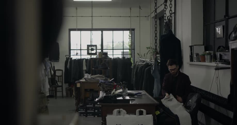 A man walks to his desk in a clothes shop and folds some trousers