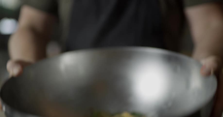 A chef shakes a mixing bowl full of a pasta and shrimp dish to mix it