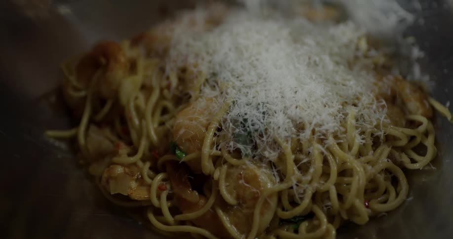 A chef shredding cheese onto a shrimp and pasta dish