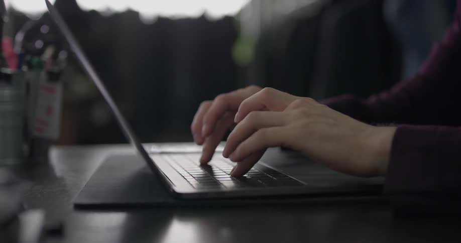 A person is sitting at a desk and is typing on their laptop computer very quickly