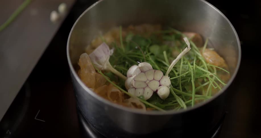 A person throws chopped garlic into a bubbling pot of cooking vegetables