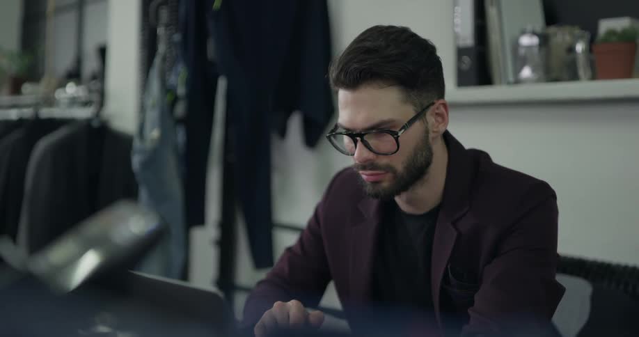 A man with a suit and glasses looking at a laptop