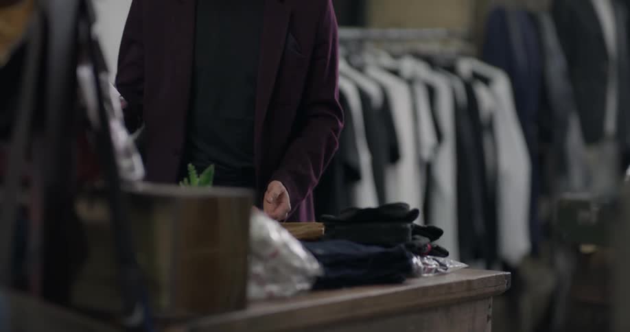 A man folds clothes on a table then picks up his phone to his ear